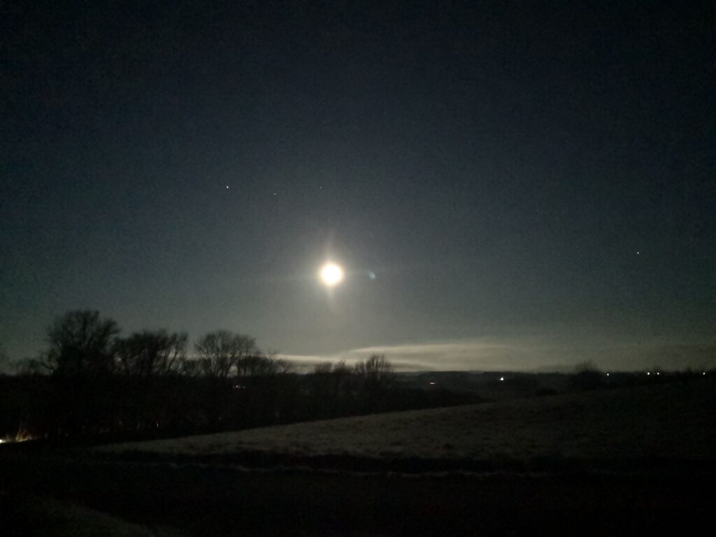 Bright full moon shines on a hilly landscape with some trees